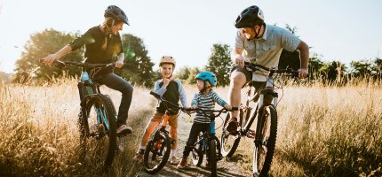 Eine junge Familie hält während ihrer Fahrradtour auf einem Feldweg.