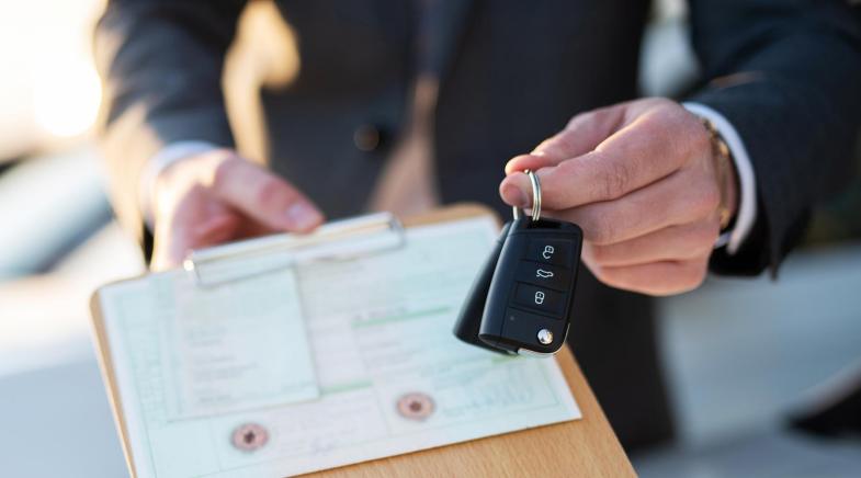 Autokauf, Verkäufer hält Zulassung Papiere und Schlüssel vor einer Reihe an Neuwagen