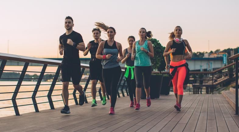 Eine Laufgruppe joggt am Wasser auf einem Steg.