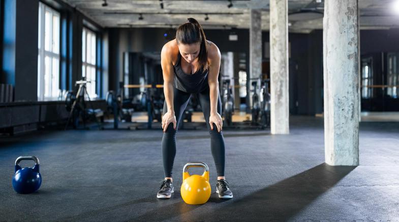 Frau steht im Fitness-Studio über eine Hantel gebeugt.