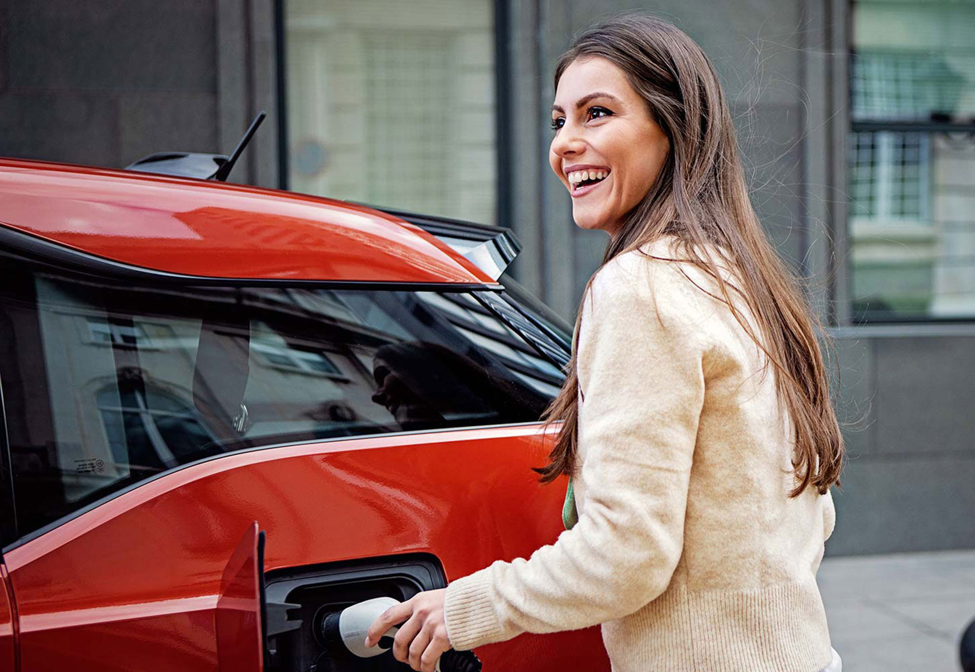 Eine Person lädt ein rotes Elektroauto an einer Ladestation auf.