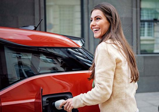 Eine Person lädt ein rotes Elektroauto an einer Ladestation auf.