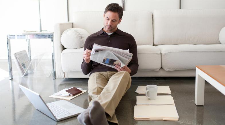 Ein Mann sitzt vor seiner Couch und liest die Tageszeitung.