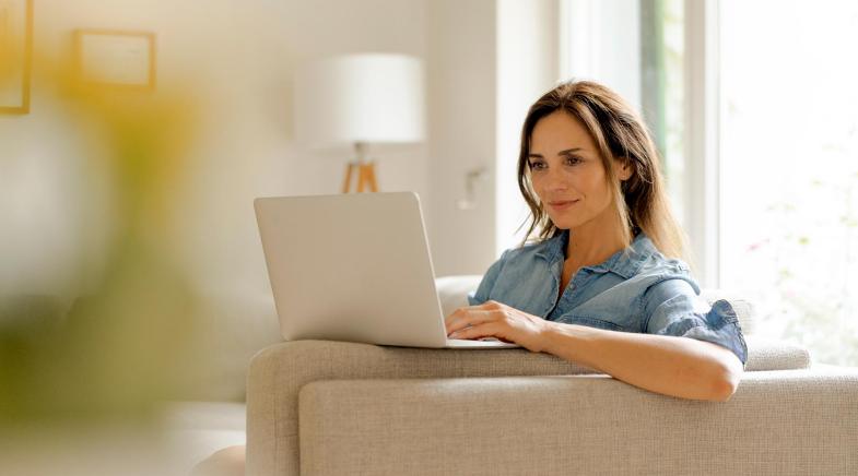 Eine Frau sitzt entspannt auf der Couch und schaut in ihren Laptop.