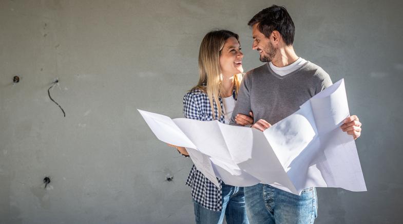 Paar steht mit Bauplan im eigenen Haus