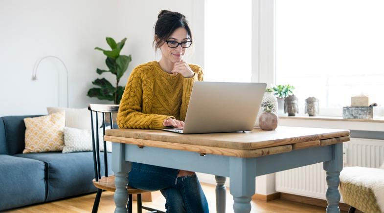 Frau mit gelbem Strickpulli und Brille sitzt vor einem Laptop.