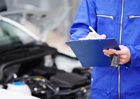 Mechaniker geht vor einem Auto eine Checkliste durch.