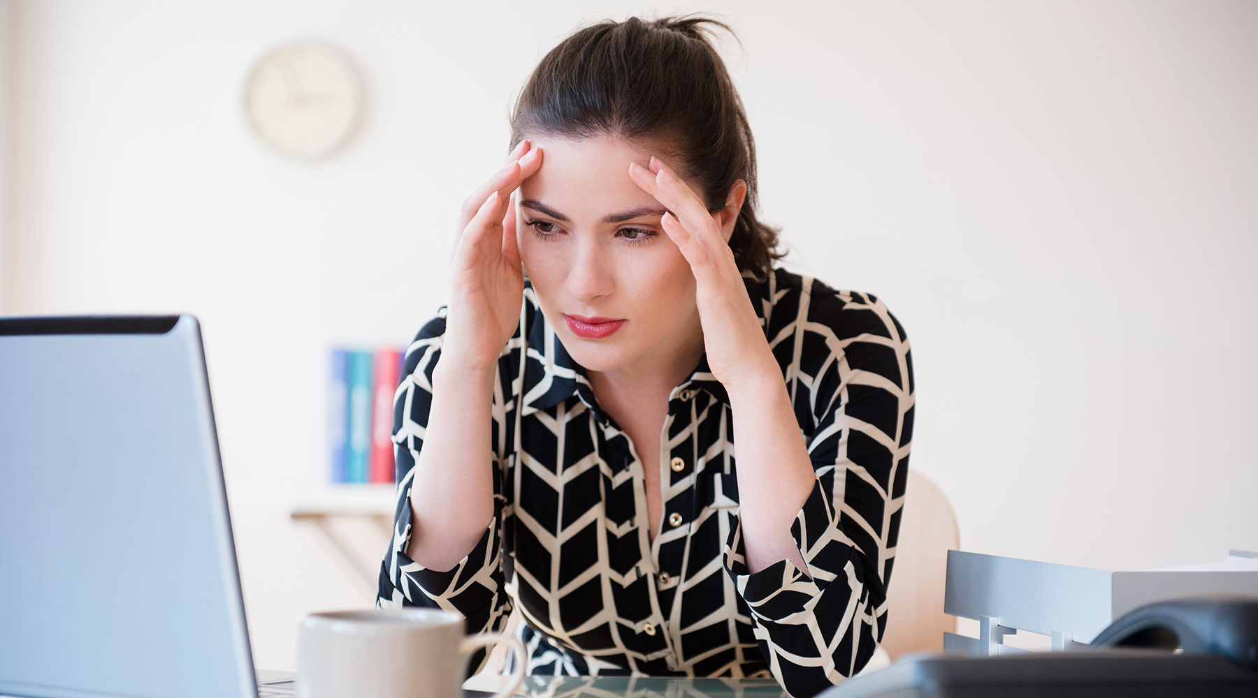 Frau im Büro fasst sich an die Schläfen.