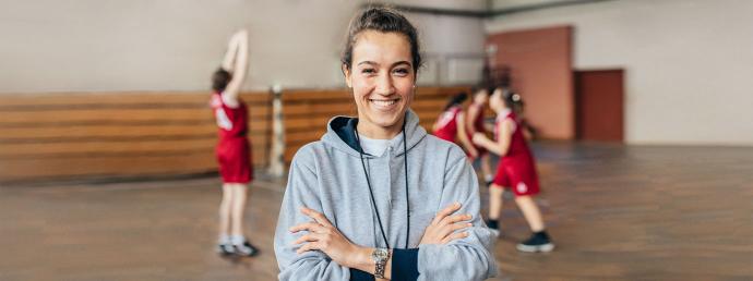 Sportlehrerin steht mit Schülern in einer Turnhalle.