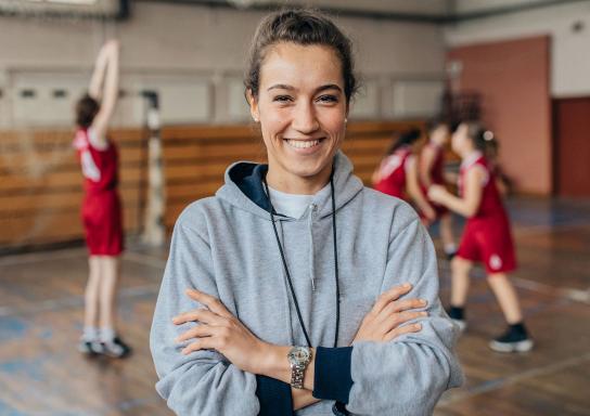 Sportlehrerin steht mit Schülern in einer Turnhalle.