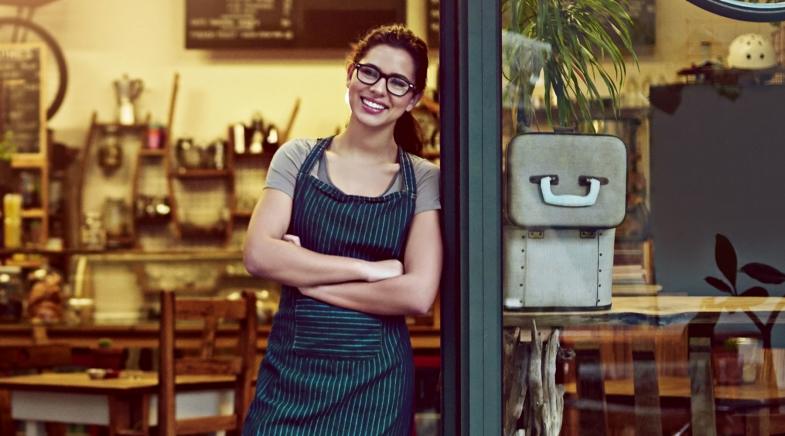 Junge Frau steht in der geöffneten Eingangstür zum Coffee Shop und wartet auf Gäste