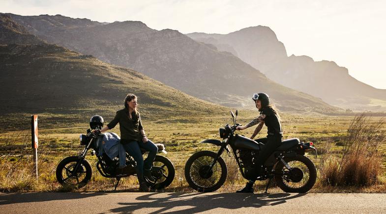 Zwei Motorradfahrer machen vor ein paar Hügeln Pause.