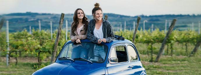 Zwei Frauen schauen aus dem Schiebedach ihres Oldtimer-Kleinwagens.