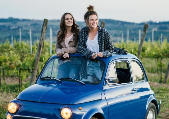 Zwei Frauen schauen aus dem Schiebedach ihres Oldtimer-Kleinwagens.