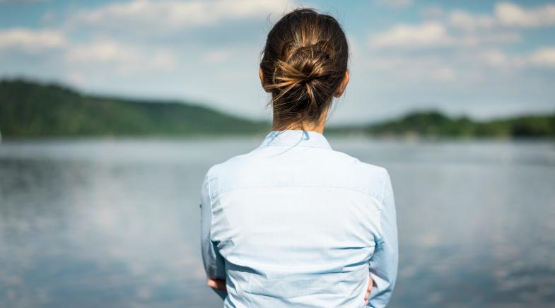 Eine Frau von hinten, die auf einen See blickt.