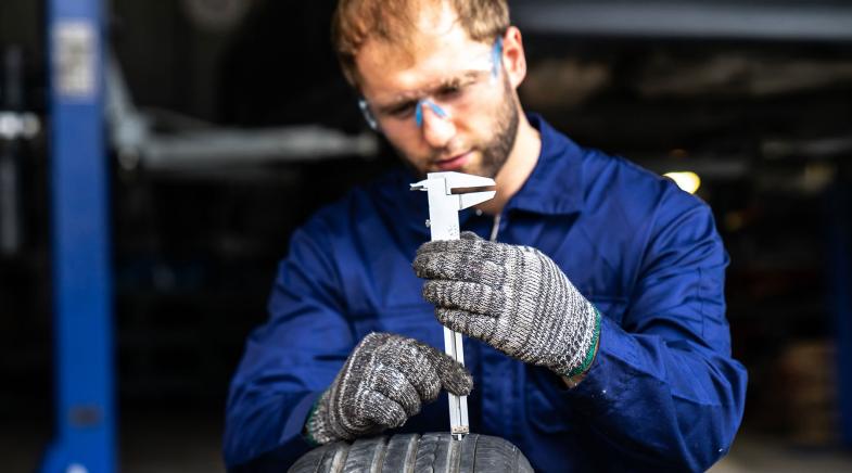 Ein Mechaniker prüft die Profiltiefe eines Autoreifens mit einem Werkzeug.