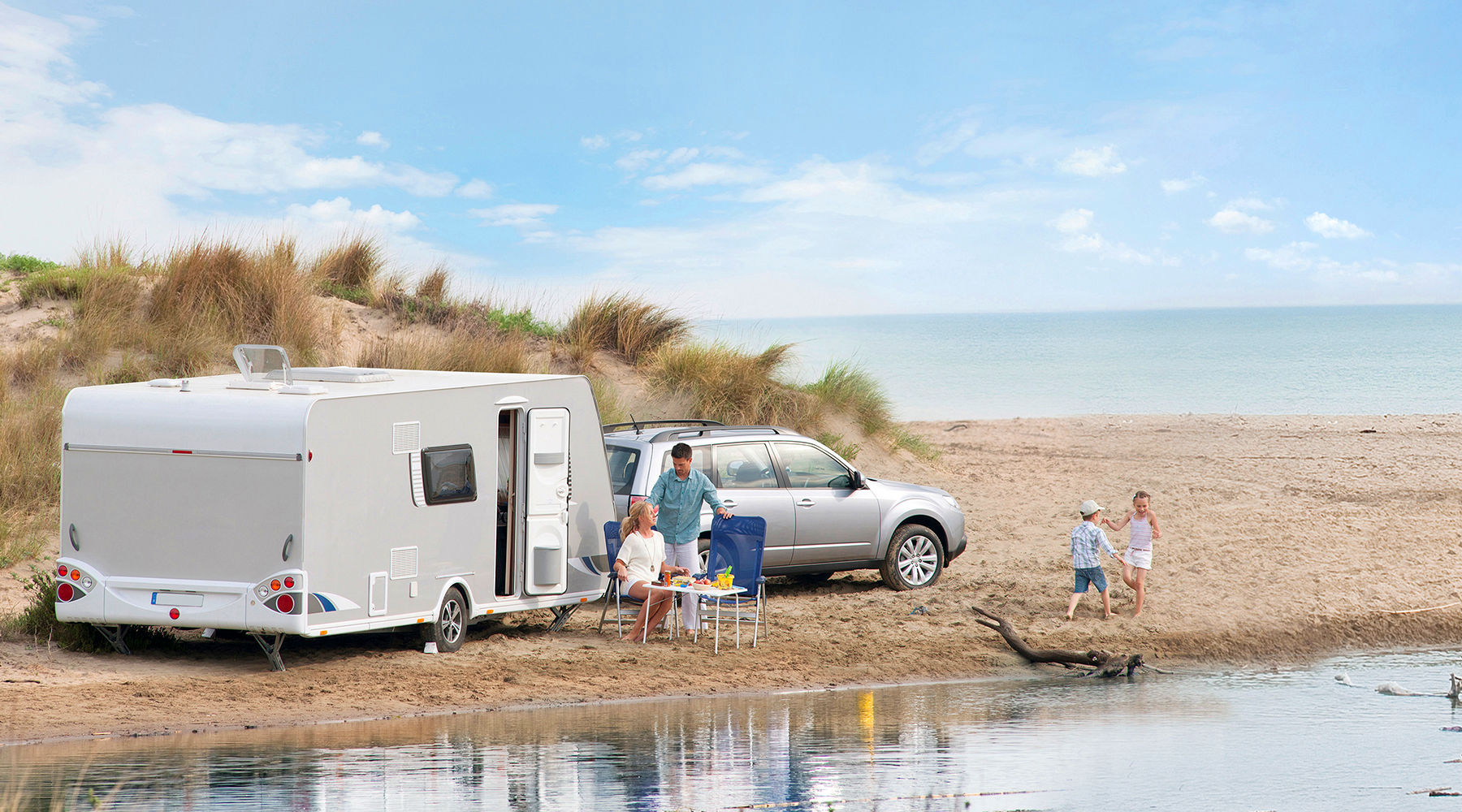 Familie mit Auto und Wohnwagen rastet am Strand.