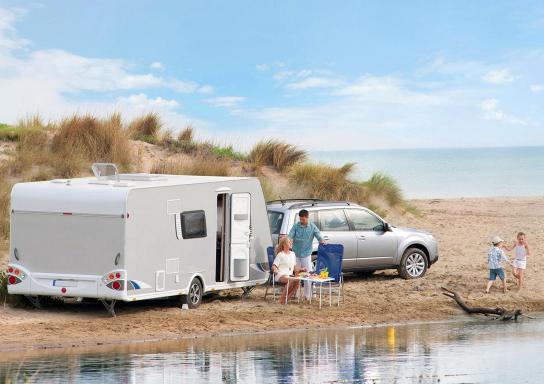 Familie mit Auto und Wohnwagen rastet am Strand.