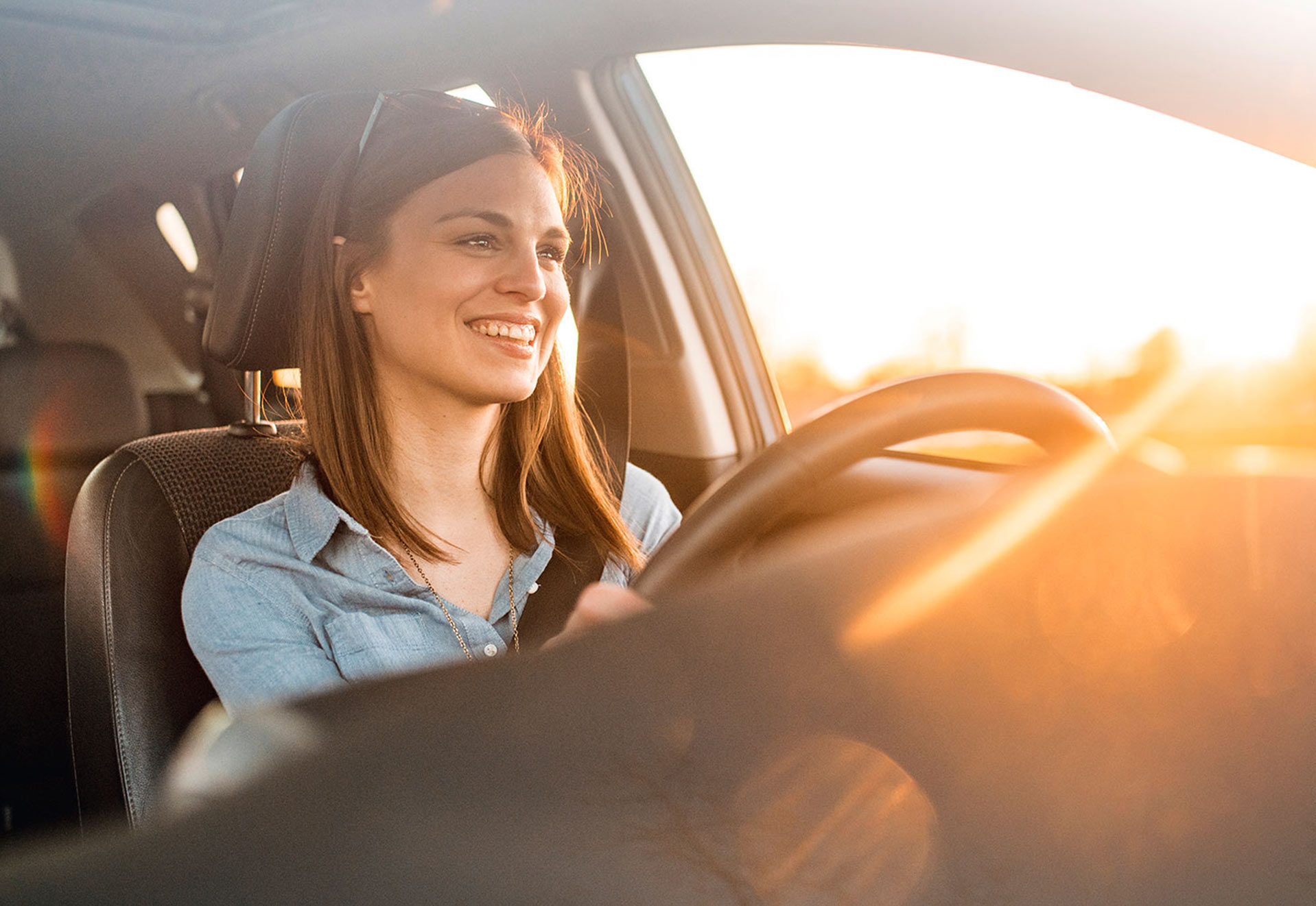 Eine Frau sitzt lächelnd im Auto und schaut in den Sonnenuntergang.