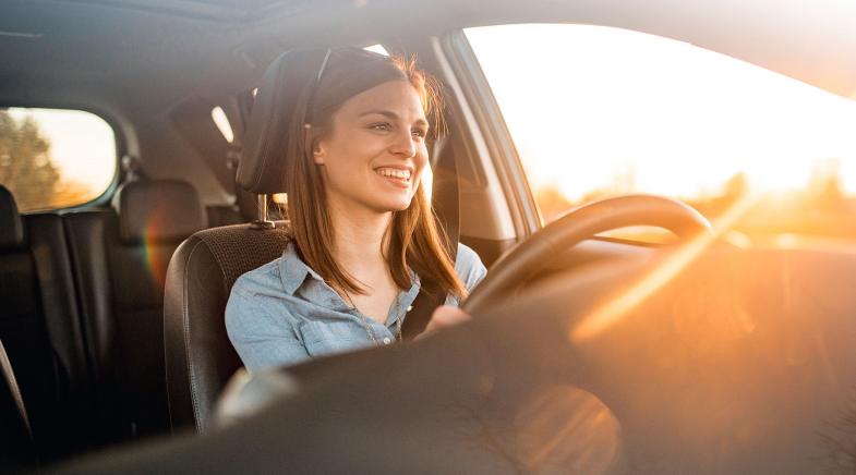 Eine Frau sitzt lächelnd im Auto und schaut in den Sonnenuntergang.