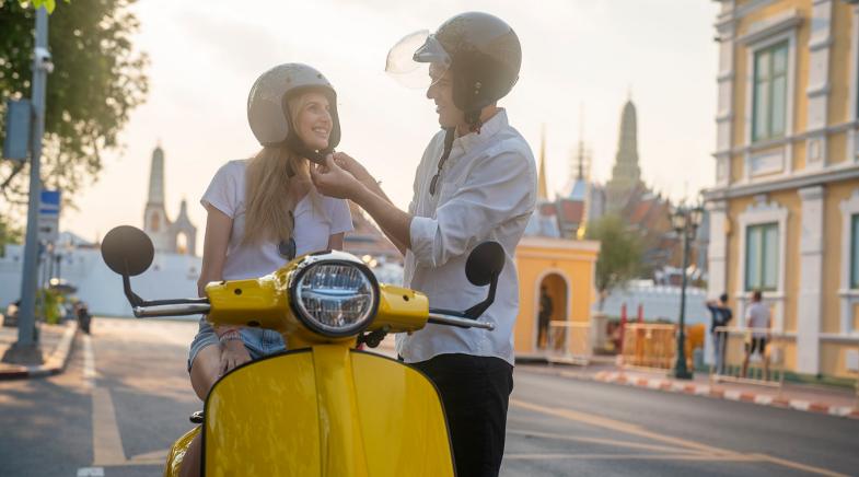 Ein Mann zieht einer Frau auf einem Motorroller einen Helm an.