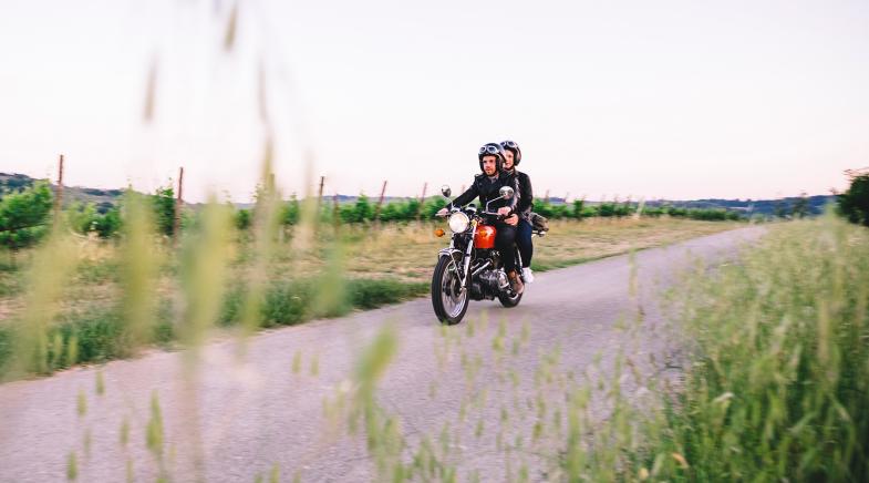 Ein Paar fährt mit einem alten Motorrad über einen Feldweg.