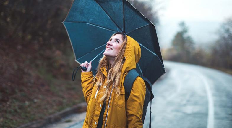 Frau mit gelber Regenjacke und schwarzem Schirm schaut nach oben.