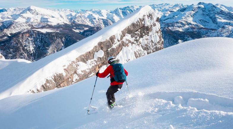 Ein Skifahrer fährt durch Tiefschnee bergab.