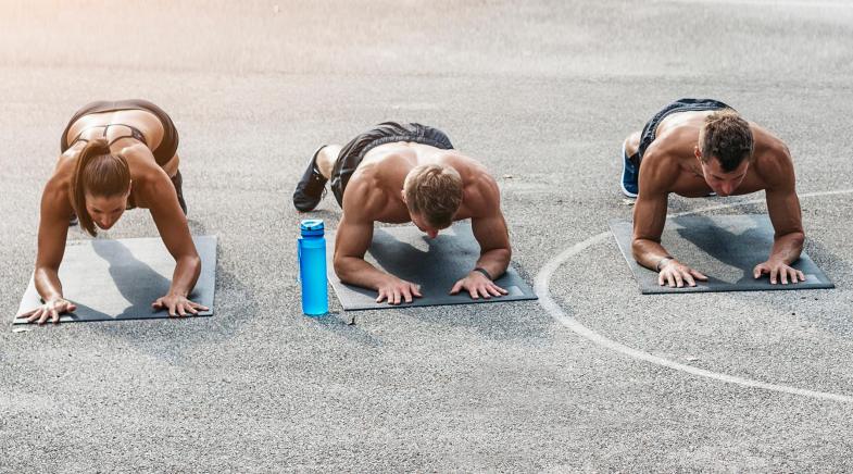 Vier Sportler machen die Planke auf Yogamatten auf einem Sportplatz.