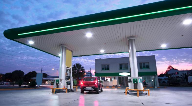 Rotes Auto fährt in der Abenddämmerung an eine Zapfsäule einer Tankstelle.