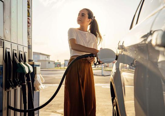 Junge Frau tankt ihr Auto an einer Tankstelle.