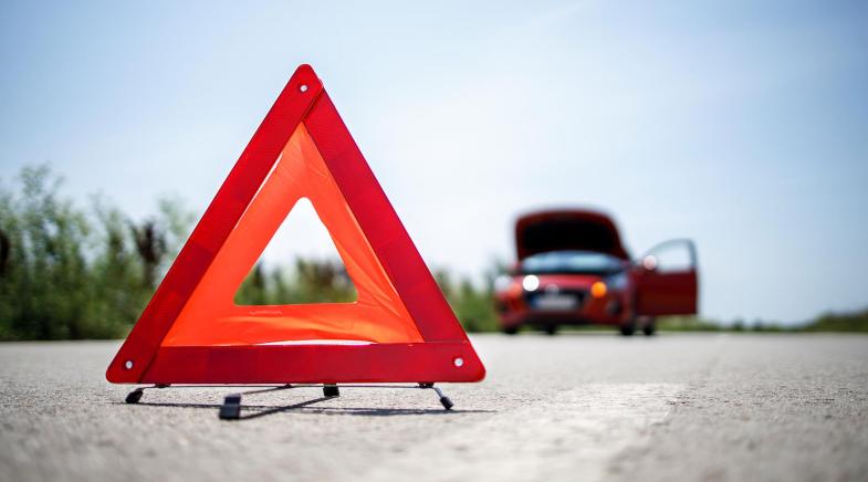 Tragbares Warndreieck auf der Straße soll auf das Pannenfahrzeug im Hintergrund aufmerksam machen.