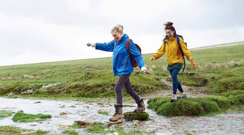 Zwei wandernde Frauen überqueren einen Bach.