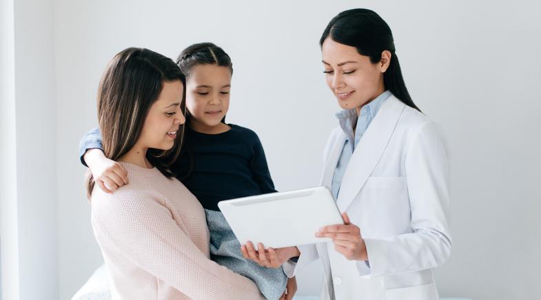 Ärtzin zeigt ihren Patienten Mutter und Tochter etwas auf dem Tablet