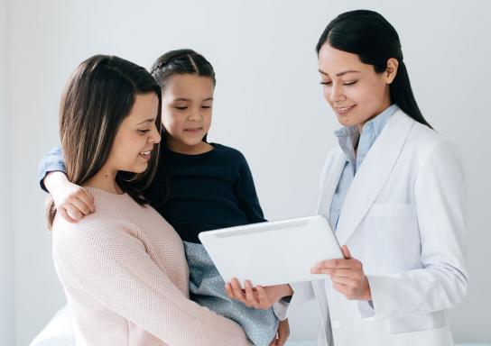 Ärtzin zeigt ihren Patienten Mutter und Tochter etwas auf dem Tablet