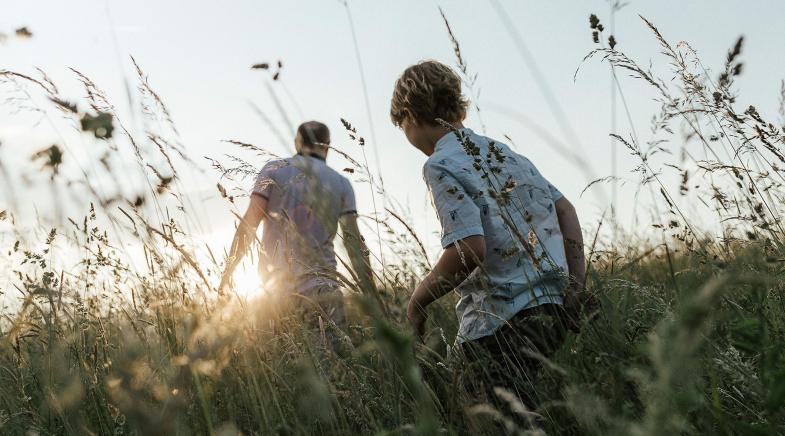 Ein Kind folgt seinem Vater durchs hohe Gras.