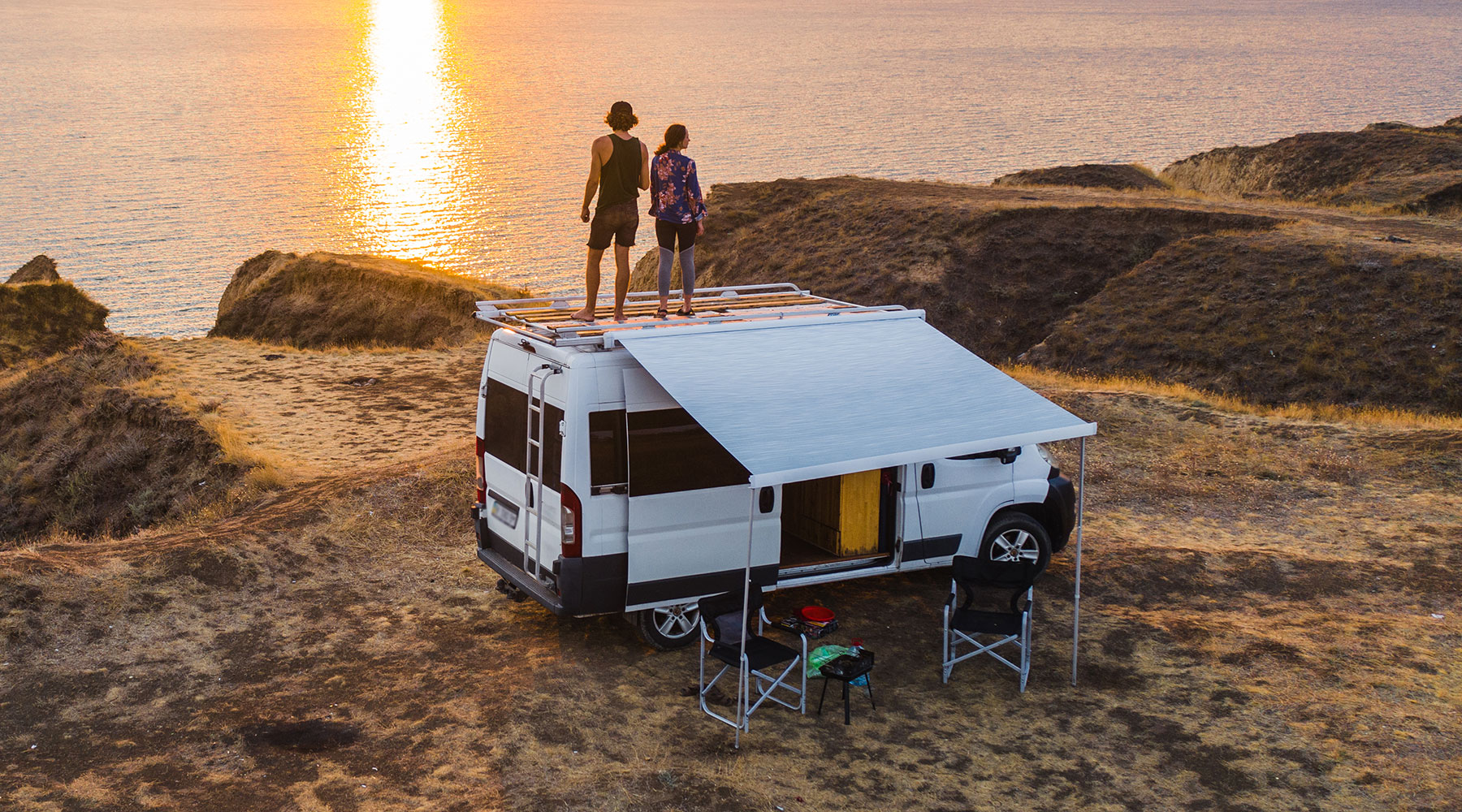 Pärchen steht auf dem Dach ihres Campers am Meer.