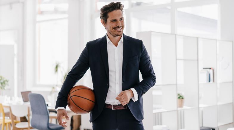 Mann im Anzug mit Basketball unter dem Arm in einer Wohnung.