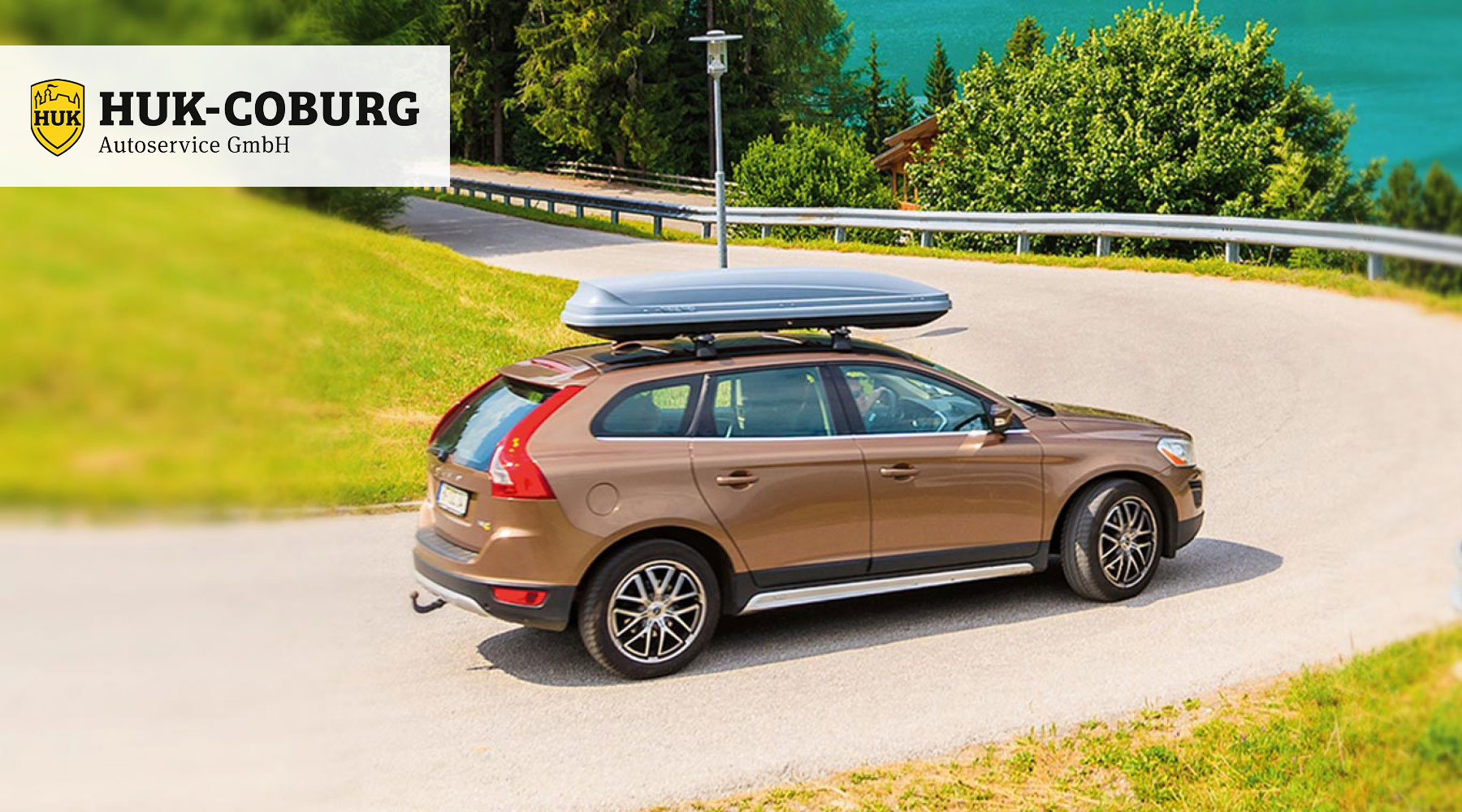Ein braunes Auto mit Dachbox fährt auf einer Landstraße. 