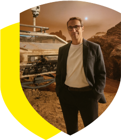 Herr Möller steht vor einem großen, staubigen Explorationsfahrzeug in einer rötlichen, felsigen Marslandschaft.