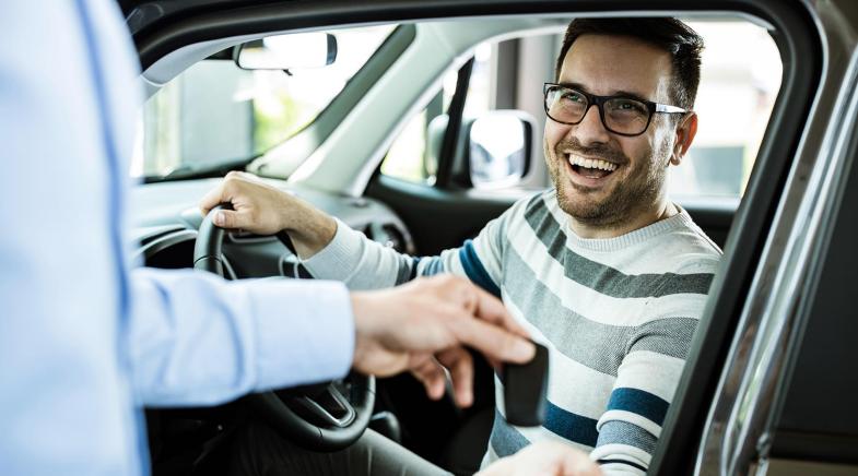 Autoverkäuferin und zwei Kunden stehen neben einem blauen Fahrzeug.