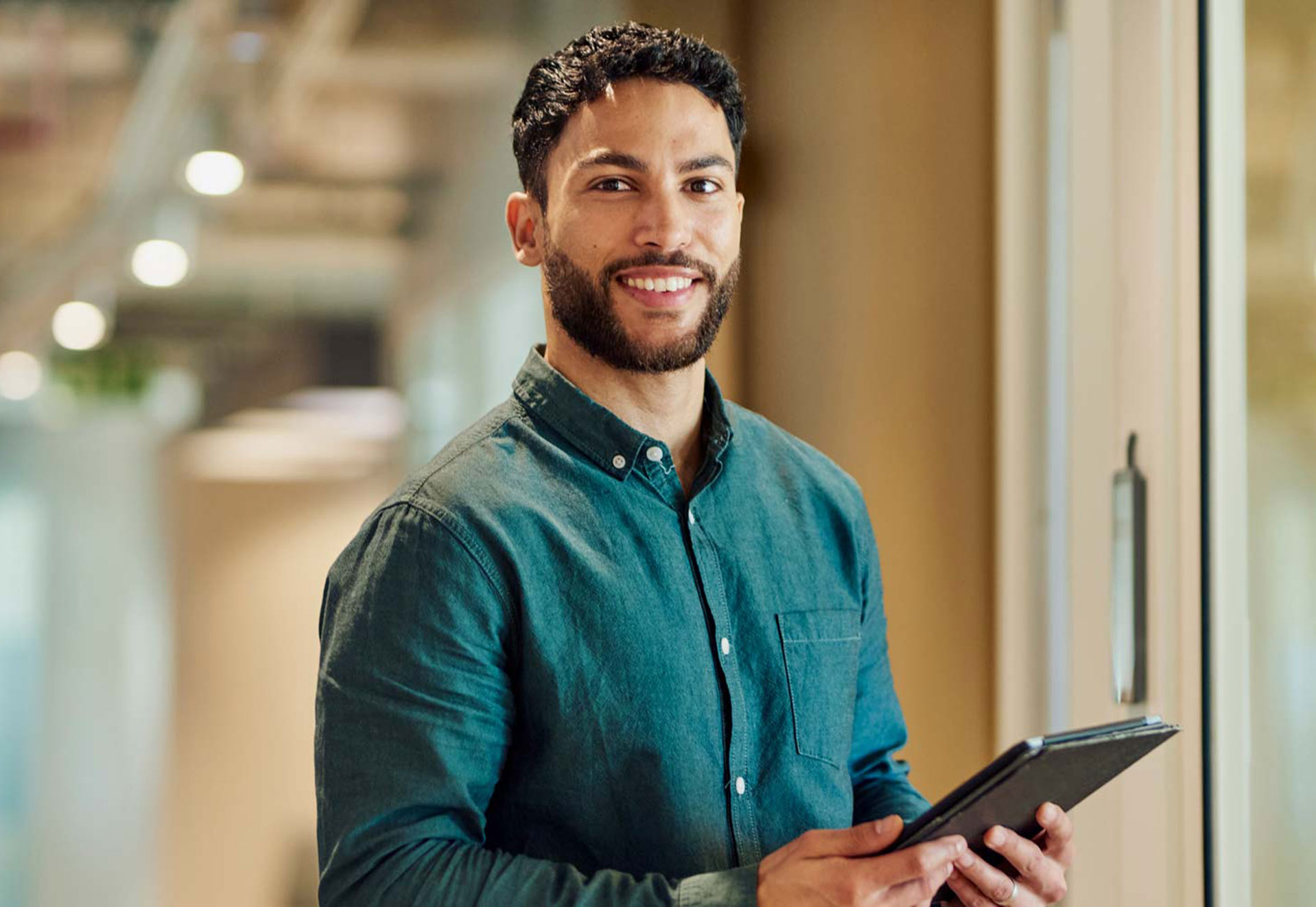 Ein Mann lächelt und hat ein iPad in der Han, im Hintergrund sieht man ein Büro.