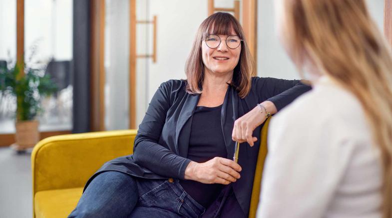 Beraterin sitzt mit einem Kunden am Tisch und zeigt ihm Vertragsunterlagen