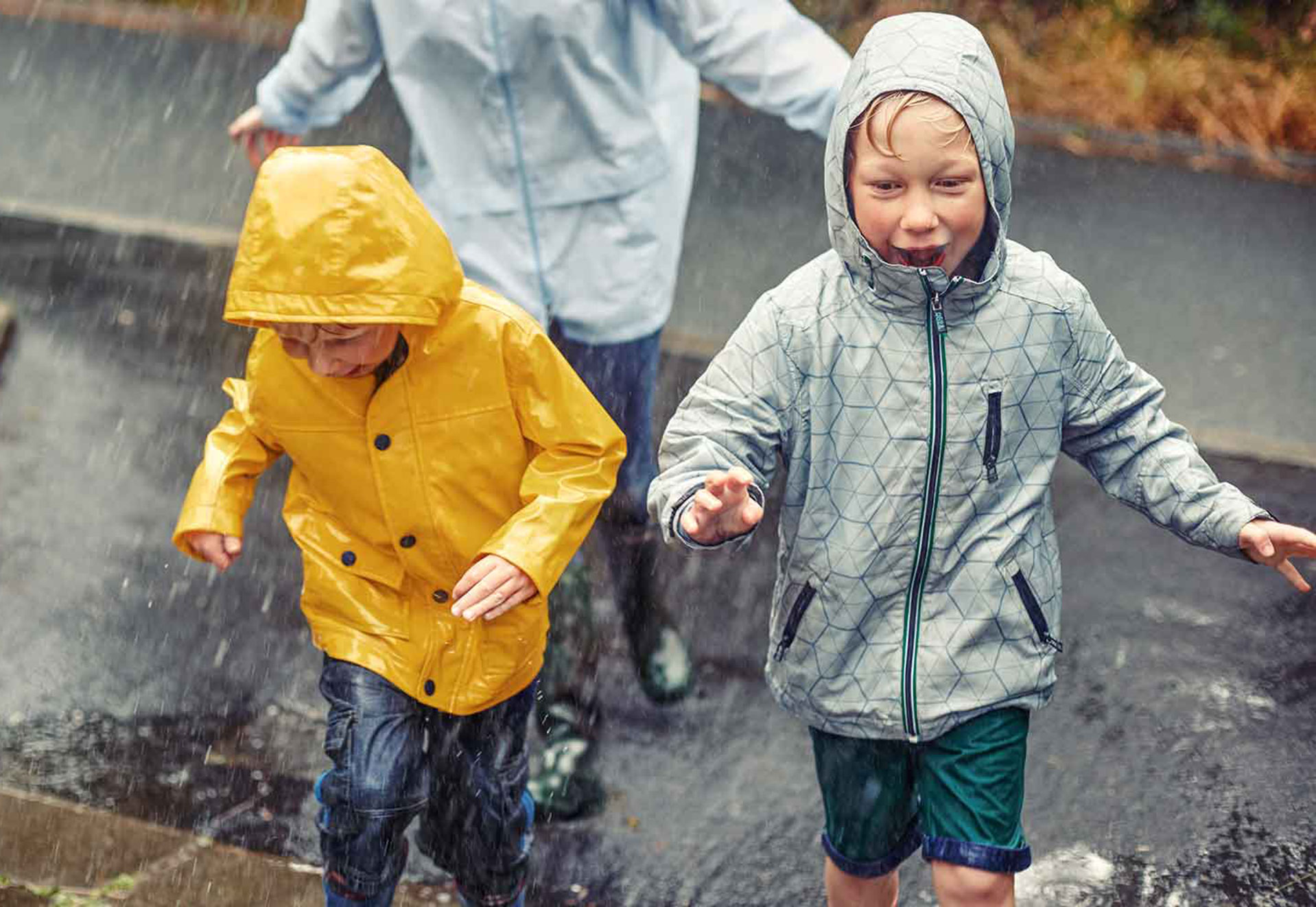 Drei Kinder rennen in Regenjacken durch den Regen