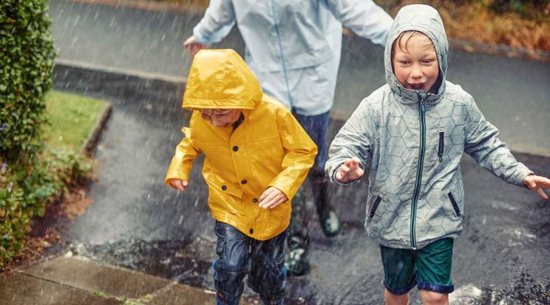 Drei Kinder rennen in Regenjacken durch den Regen