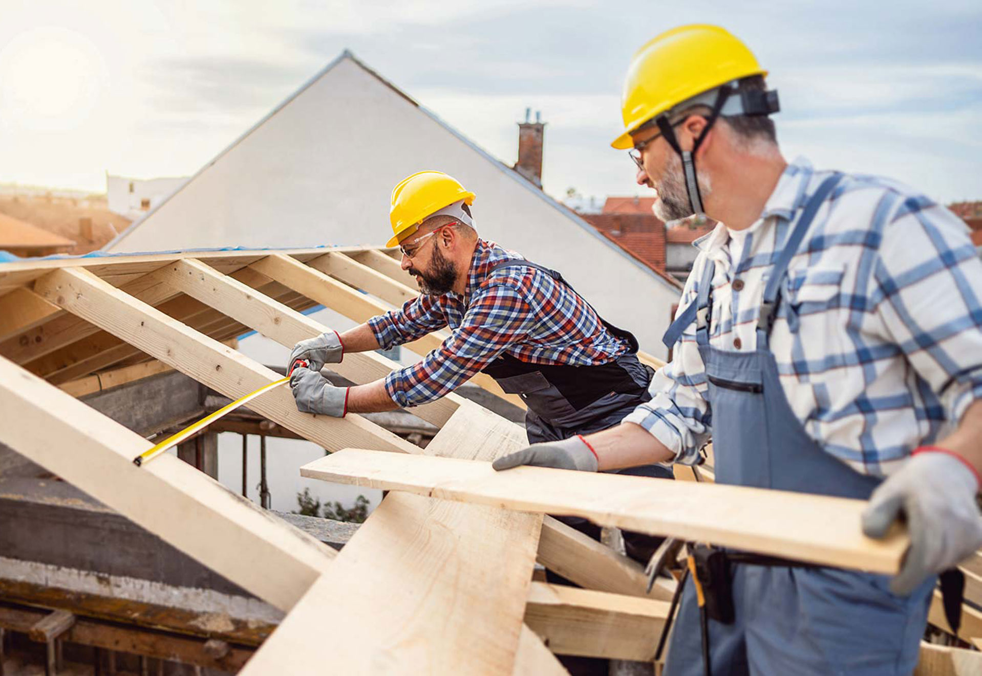 Zwei Handwerker mit Helmen stehen auf einem Haus und reparieren den Dachstuhl mit Holzbalken