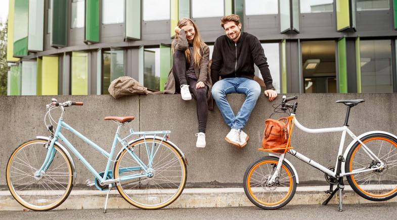 Junges Paar sitzt auf einer Mauer an der zwei Fahrräder lehnen.