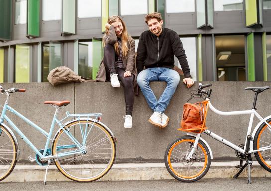 Junges Paar sitzt auf einer Mauer an der zwei Fahrräder lehnen.