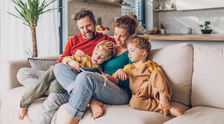 Familie mit zwei Kindern sitzt auf dem Sofa und schaut auf ein Tablet.