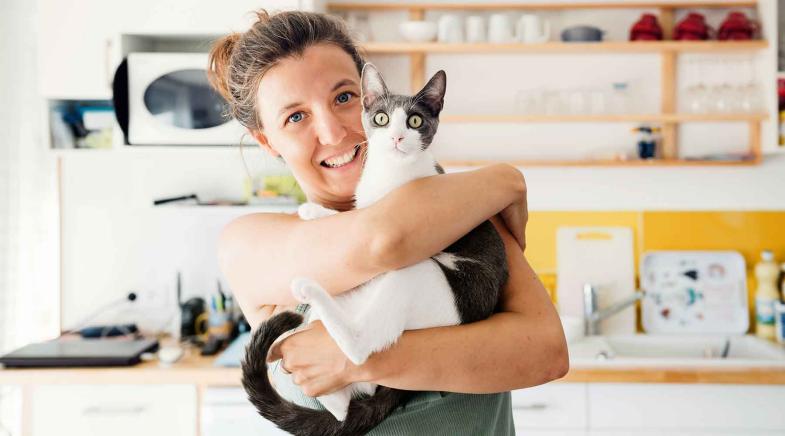 Frau hebt in der Küche ihre Katze hoch.